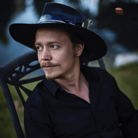 A Man Wearing A Cowboy Hat Is Sitting In A Chair With The Letter B Visible GIF