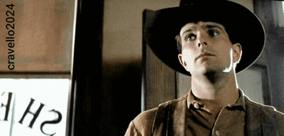 A Man Wearing A Cowboy Hat Is Standing In Front Of A Sign That Says 1H2 GIF