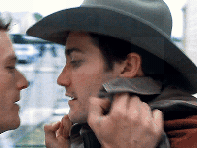 A Man Wearing A Cowboy Hat Is Touching The Face Of Another Man GIF