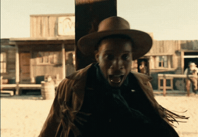 A Man Wearing A Cowboy Hat Stands In Front Of A Building With The Letter M On The Front GIF