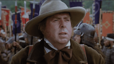A Man Wearing A Cowboy Hat Stands In Front Of A Crowd Of People GIF