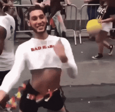 A Man Wearing A Crop Top And Shorts Is Dancing In A Crowd . GIF