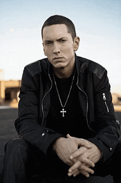 A Man Wearing A Cross Necklace Is Sitting With His Hands Folded GIF