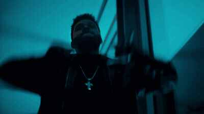 A Man Wearing A Cross Necklace Is Standing In A Dark Room GIF
