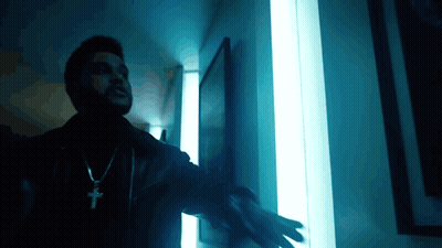 A Man Wearing A Cross Necklace Is Standing In Front Of A Blue Light GIF
