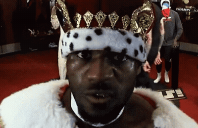 A Man Wearing A Crown And A Fur Coat Is Standing In Front Of A Sign That Says Champi GIF