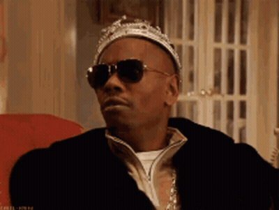 A Man Wearing A Crown And Sunglasses Is Sitting On A Chair . GIF