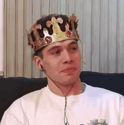 A Man Wearing A Crown Is Sitting On A Couch With Headphones . GIF