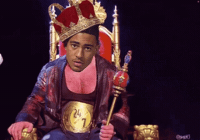 A Man Wearing A Crown Is Sitting On A Throne With A Belt That Says 24 7 GIF