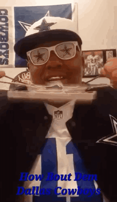 A Man Wearing A Dallas Cowboys Hat , Sunglasses , And A Cowboys Jersey Is Eating Food . GIF