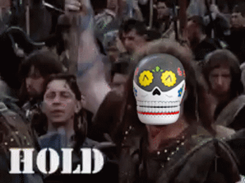 A Man Wearing A Day Of The Dead Mask Stands In Front Of A Crowd Of People With The Word Hold Below Him GIF