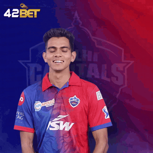 A Man Wearing A Delhi Capitals Shirt Stands In Front Of A Blue And Red Background GIF