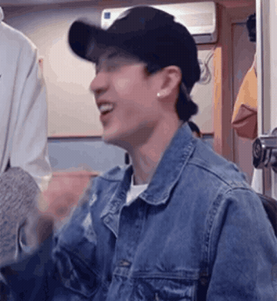 A Man Wearing A Denim Jacket And A Baseball Cap Is Smiling And Laughing . GIF