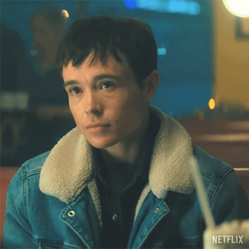 A Man Wearing A Denim Jacket And A Sherpa Collar Is Sitting At A Table With A Drink In His Hand . GIF