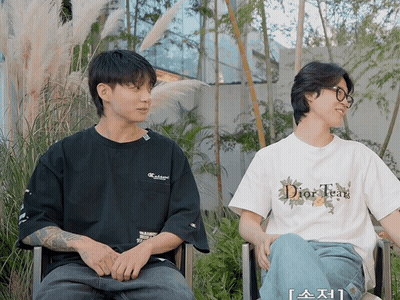 A Man Wearing A Dior Tear T-Shirt Sits Next To A Man Wearing A Black Shirt GIF