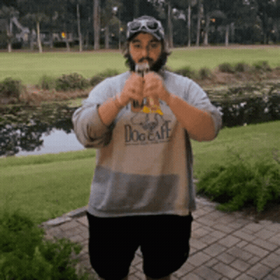 A Man Wearing A Dog Cafe Shirt Is Standing In Front Of A Golf Course GIF