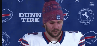 A Man Wearing A Dunn Tire Hat Stands In Front Of A Blue Background GIF