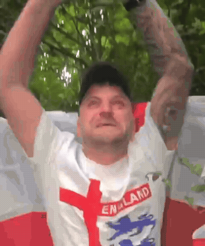 A Man Wearing A England Shirt Is Holding His Arms Up In The Air . GIF