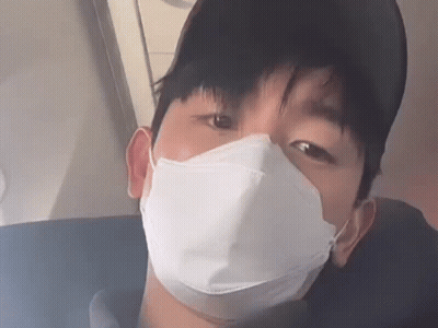 A Man Wearing A Face Mask And A Baseball Cap Is Sitting On A Plane . GIF
