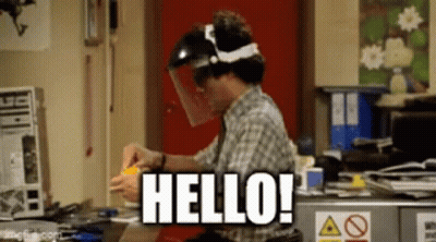 A Man Wearing A Face Shield Is Sitting At A Desk And Says Hello . GIF