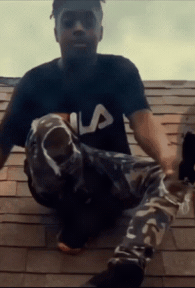 A Man Wearing A Fila Shirt Sits On A Rooftop GIF