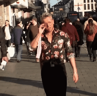 A Man Wearing A Floral Shirt Is Walking Down A Street GIF