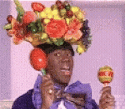 A Man Wearing A Flowered Hat Is Holding A Lollipop In His Hand . GIF