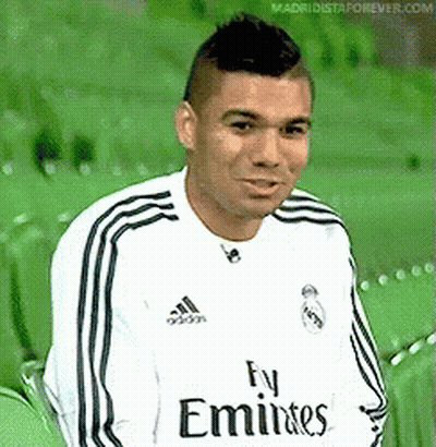 A Man Wearing A Fly Emirates Jersey Is Sitting On A Green Chair . GIF