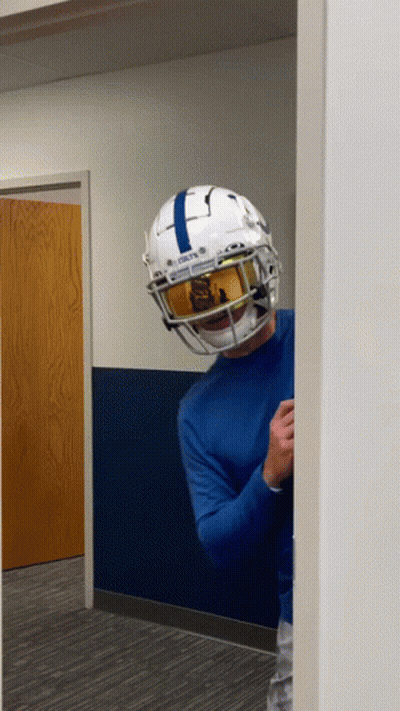 A Man Wearing A Football Helmet And Goggles Is Standing In A Hallway . GIF
