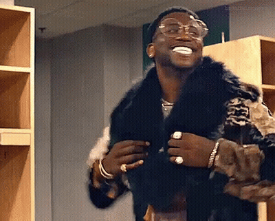 A Man Wearing A Fur Coat And Glasses Is Standing In A Locker Room . GIF