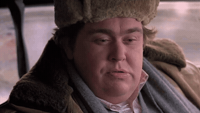 A Man Wearing A Fur Hat And Scarf Is Sitting In A Car And Looking At The Camera . GIF