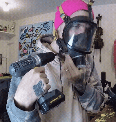 A Man Wearing A Gas Mask Is Holding A Drill In His Hand GIF