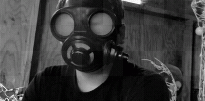 A Man Wearing A Gas Mask Looks At The Camera In A Black And White Photo GIF