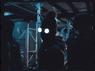 A Man Wearing A Gas Mask Stands In A Dark Room With Chinese Writing On The Bottom Right GIF