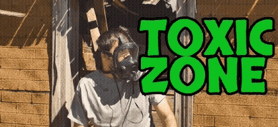 A Man Wearing A Gas Mask Stands In Front Of A Sign That Reads Toxic Zone GIF