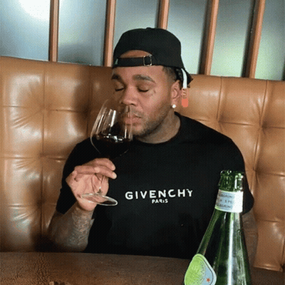A Man Wearing A Givenchy Shirt Is Drinking Wine GIF