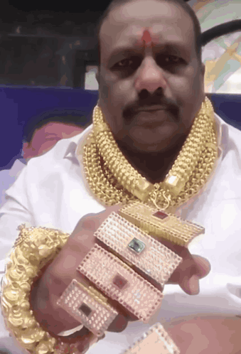 A Man Wearing A Gold Necklace And Bracelets Is Holding A Bracelet That Says ' A ' GIF