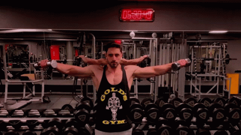 A Man Wearing A Gold 'S Gym Tank Top Is Lifting Dumbbells In A Gym GIF