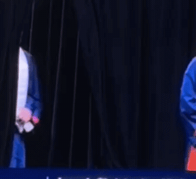 A Man Wearing A Graduation Cap And Gown Is Dancing On A Stage . GIF
