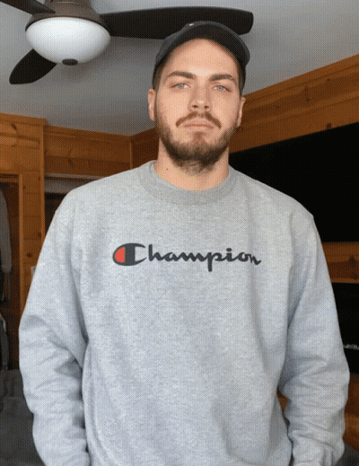 A Man Wearing A Gray Champion Sweatshirt Stands In Front Of A Ceiling Fan GIF