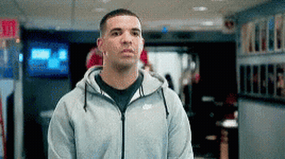 A Man Wearing A Gray Nike Hoodie Is Standing In A Hallway . GIF