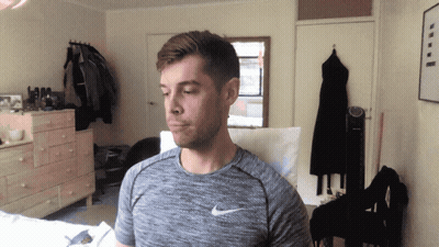 A Man Wearing A Gray Nike Shirt Stands In A Bedroom GIF