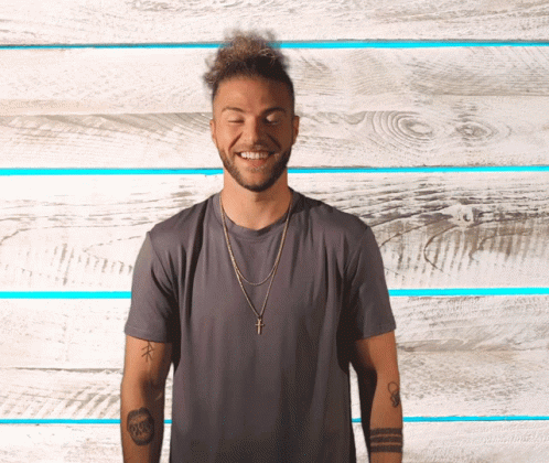 A Man Wearing A Gray Shirt And A Gold Cross Necklace Smiles With His Eyes Closed GIF