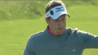A Man Wearing A Gray Sweater And A White Hat Is Standing On A Golf Course . GIF