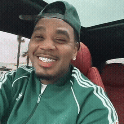 A Man Wearing A Green Adidas Jacket And A Green Hat Is Smiling While Sitting In A Car . GIF