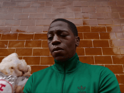 A Man Wearing A Green Adidas Jacket Eating A Hot Dog GIF