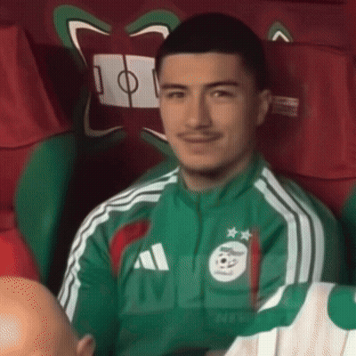 A Man Wearing A Green Adidas Jacket Is Sitting In A Chair GIF