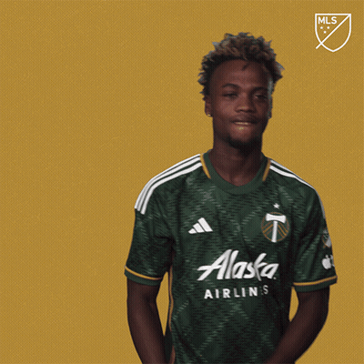 A Man Wearing A Green Alaska Shirt Stands In Front Of A Gold Background GIF