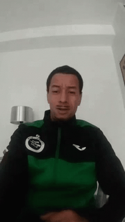 A Man Wearing A Green And Black Jacket Is Making A Face . GIF