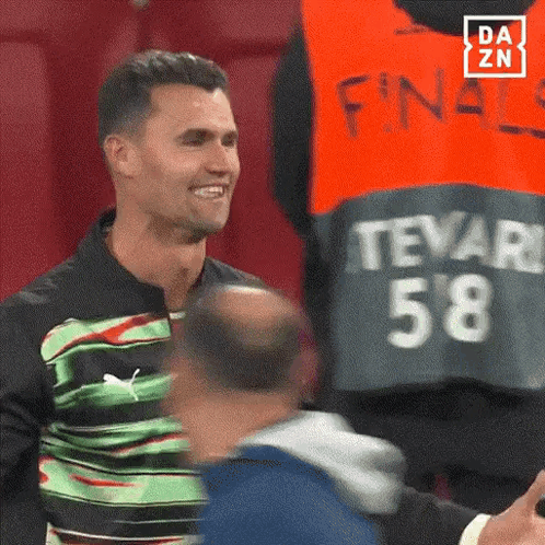 A Man Wearing A Green And Black Shirt With The Number 58 On It Is Smiling . GIF